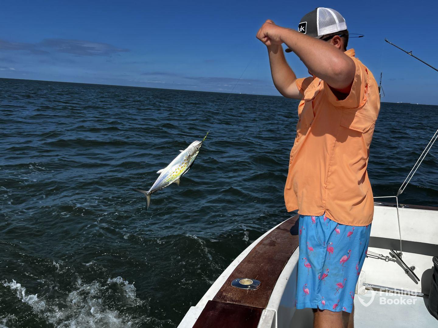 A young angler reeling in a vibrant Mahi Mahi while fishing on a sunny day in open waters.