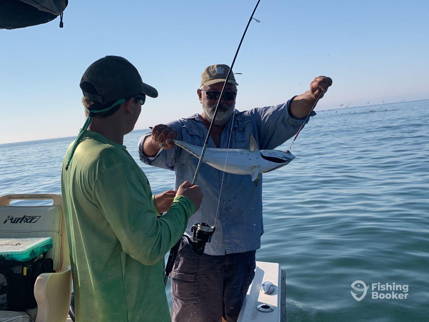 A young angler and an experienced fisherman enjoying a successful catch of a small fish while out on the water.