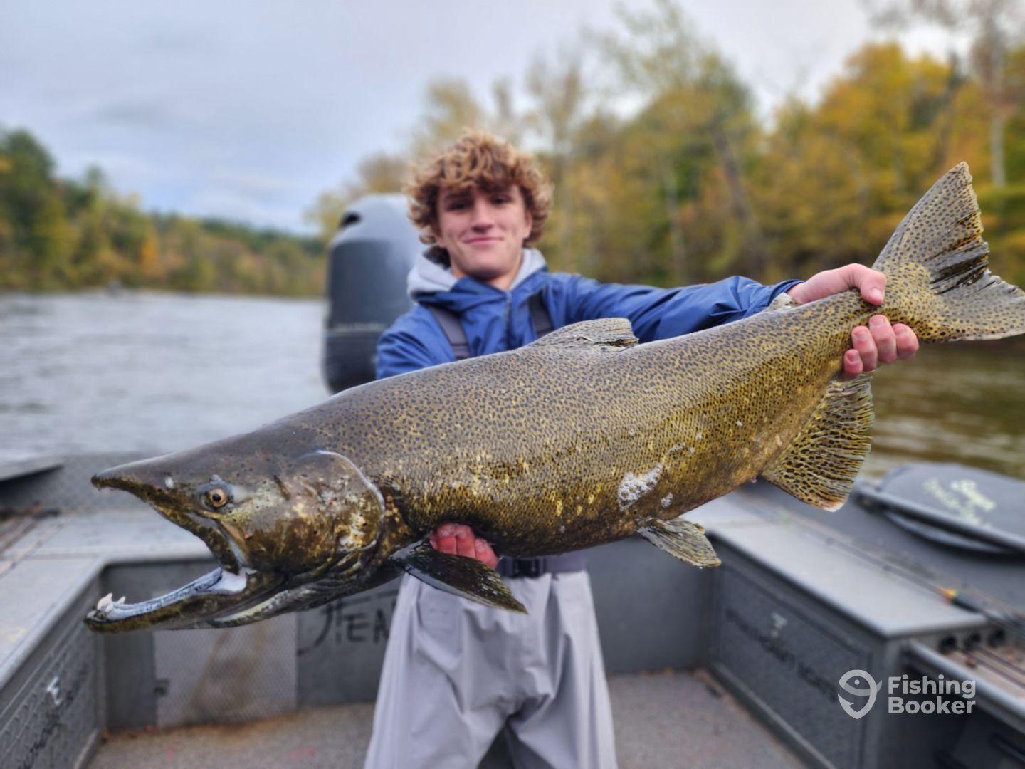 A young angler proudly displaying a large Salmon while fishing on a scenic river during autumn.