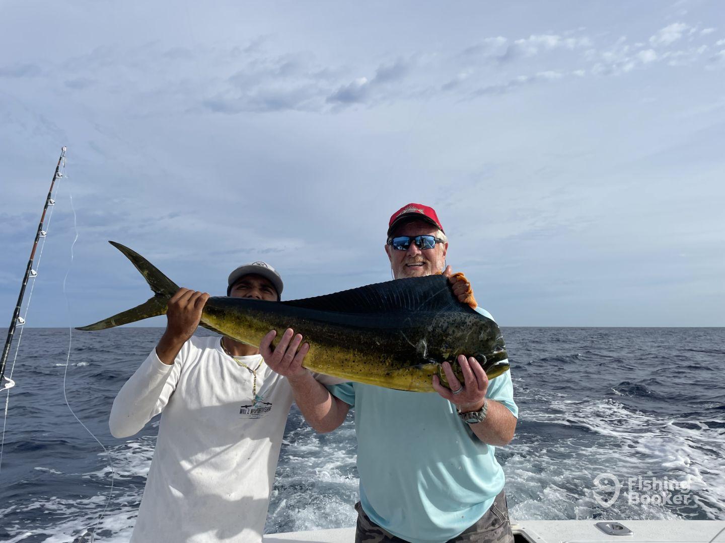 Two anglers proudly displaying a large Mahi Mahi while out on the open ocean, showcasing a successful fishing trip.