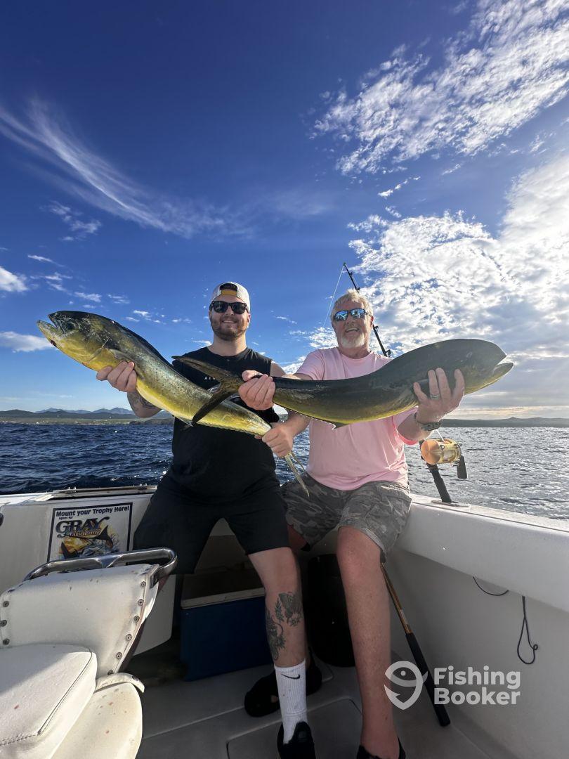 Two anglers proudly displaying their catch of Mahi Mahi while aboard a fishing boat, enjoying a sunny day on the water.
