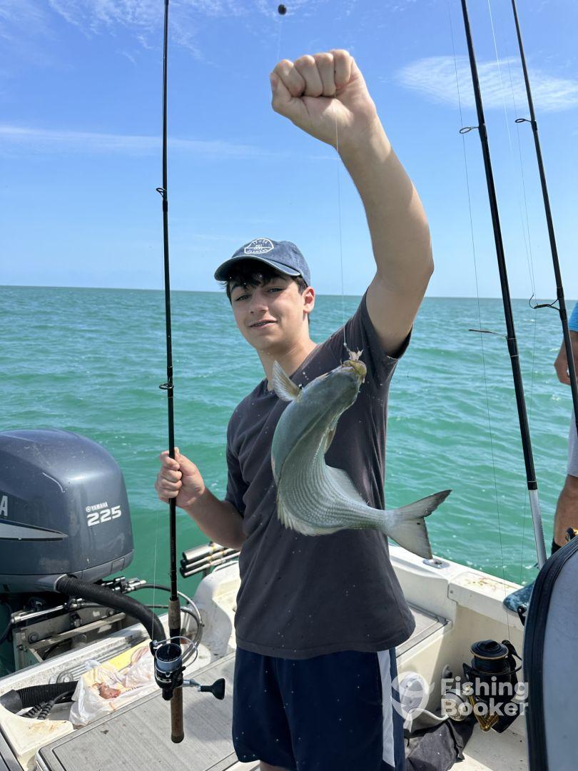 A young angler proudly displaying a freshly caught fish while fishing on a boat in clear waters.