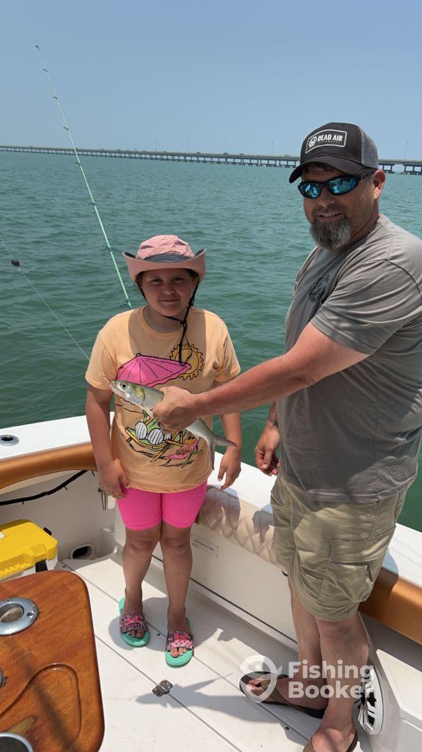 A young angler proudly holding a small fish with an adult on a boat, enjoying a fishing trip in calm waters.
