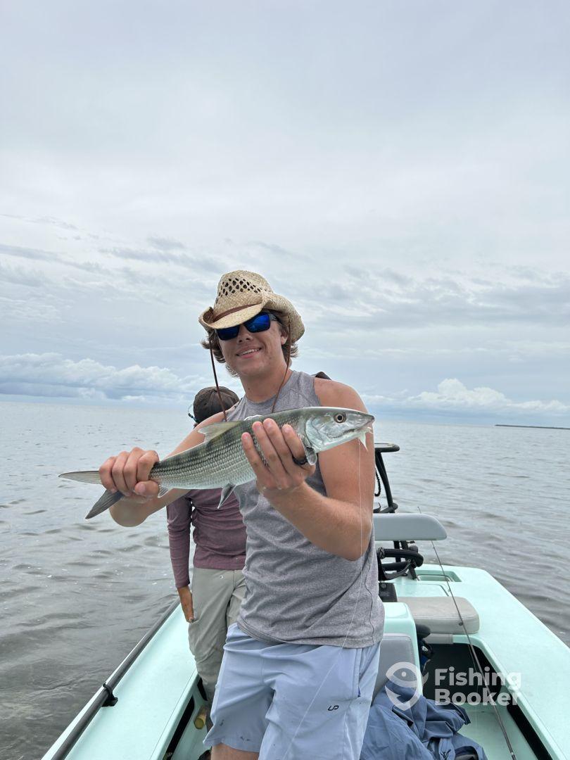 A young angler proudly displaying a striped bass while fishing from a boat on a calm day.