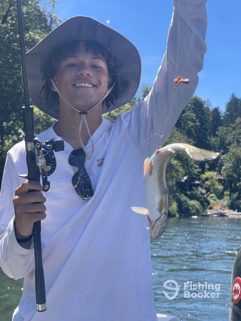 A young angler joyfully displaying a freshly caught fish while fishing on a scenic river, showcasing a sunny day and a relaxed fishing environment.