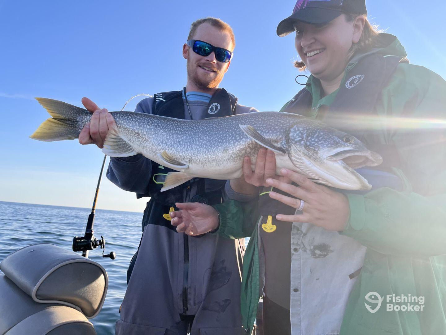 Two anglers proudly displaying a large Northern Pike while fishing on a calm lake, showcasing their successful catch.