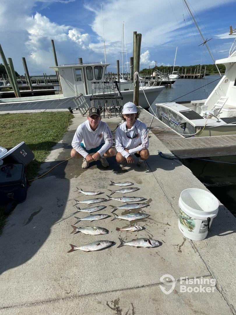 Two young anglers displaying a variety of fish, including Spanish Mackerel, laid out on the dock after a successful fishing trip.
