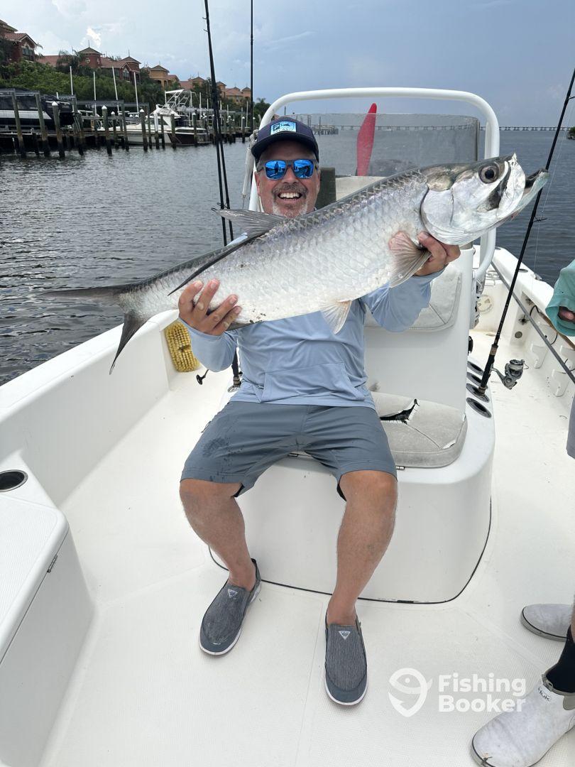 An enthusiastic angler proudly displaying a large Tarpon while seated on a fishing boat, showcasing a successful day on the water.