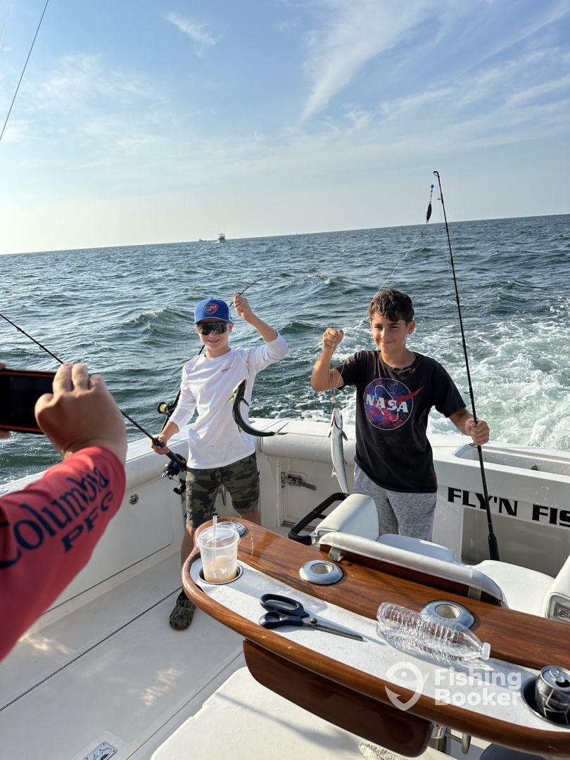 Two young anglers excitedly reeling in their catch while fishing on a charter boat, showcasing a lively day on the water.