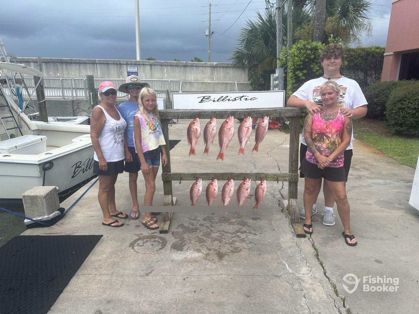 A family poses proudly in front of a catch board displaying several Red Snapper after a successful fishing trip.