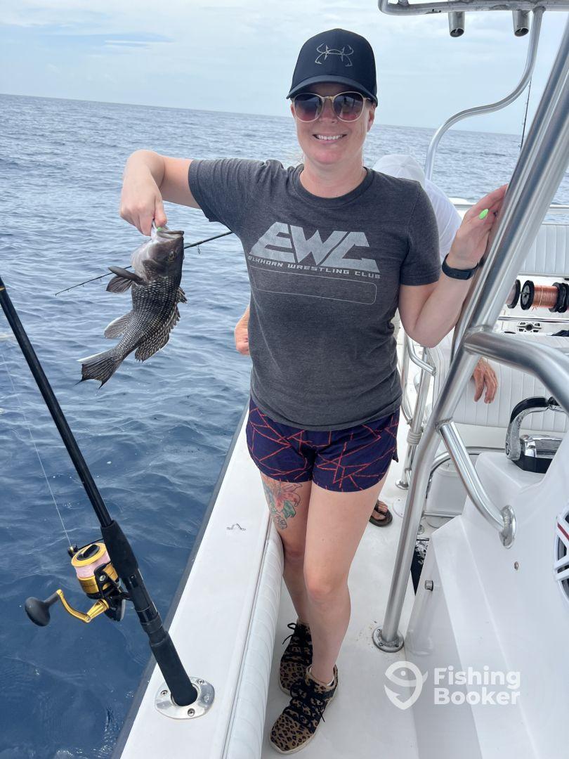 An angler proudly displaying a Black Grouper while fishing on a charter boat in open waters.