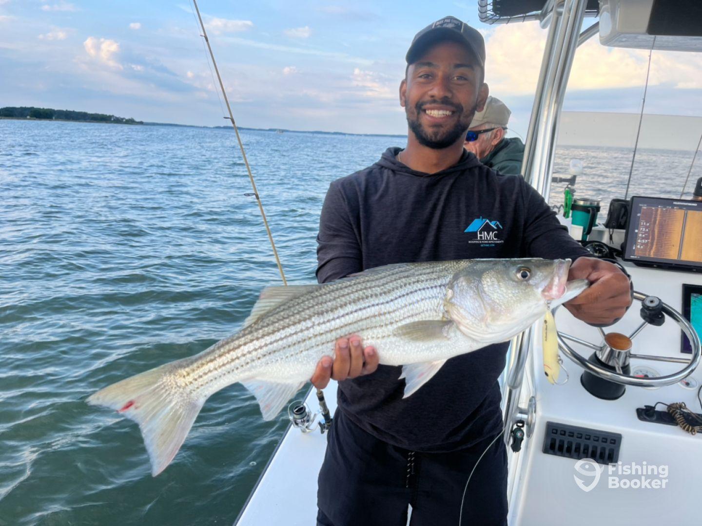 Angler proudly displaying a striped bass while fishing on a boat, showcasing the excitement of a successful catch.