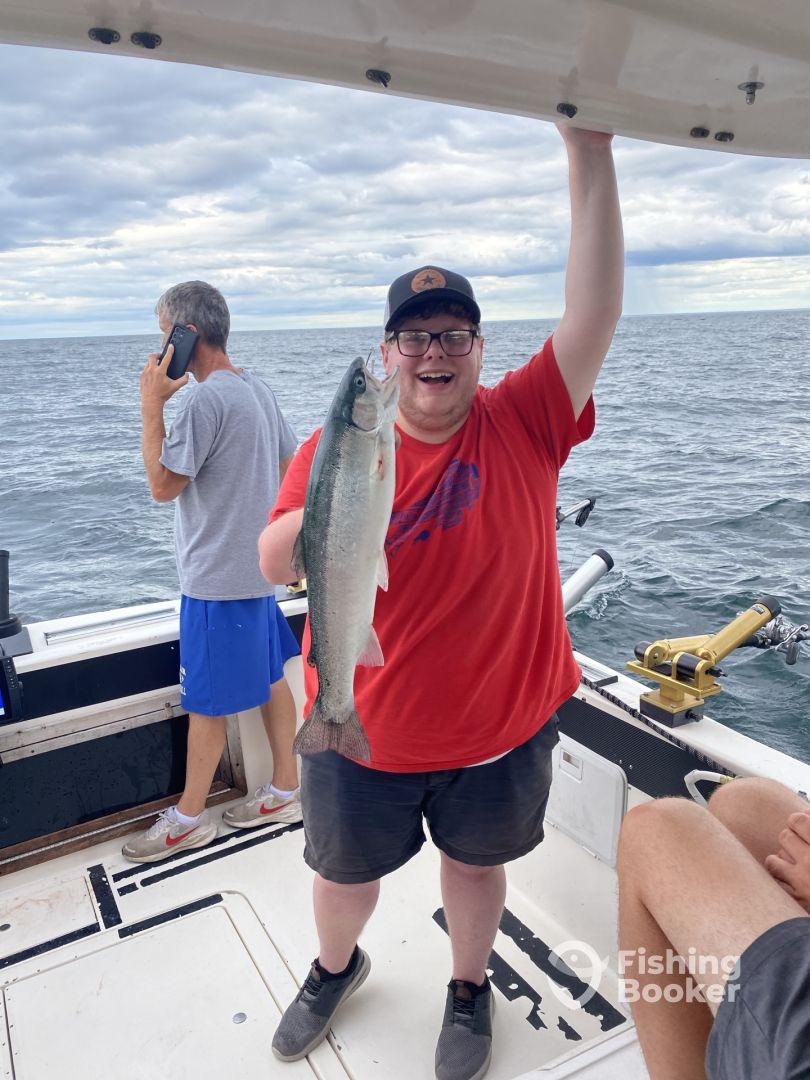 A happy angler proudly displaying a freshly caught Salmon aboard a fishing boat, with fellow anglers in the background enjoying the day on the water.