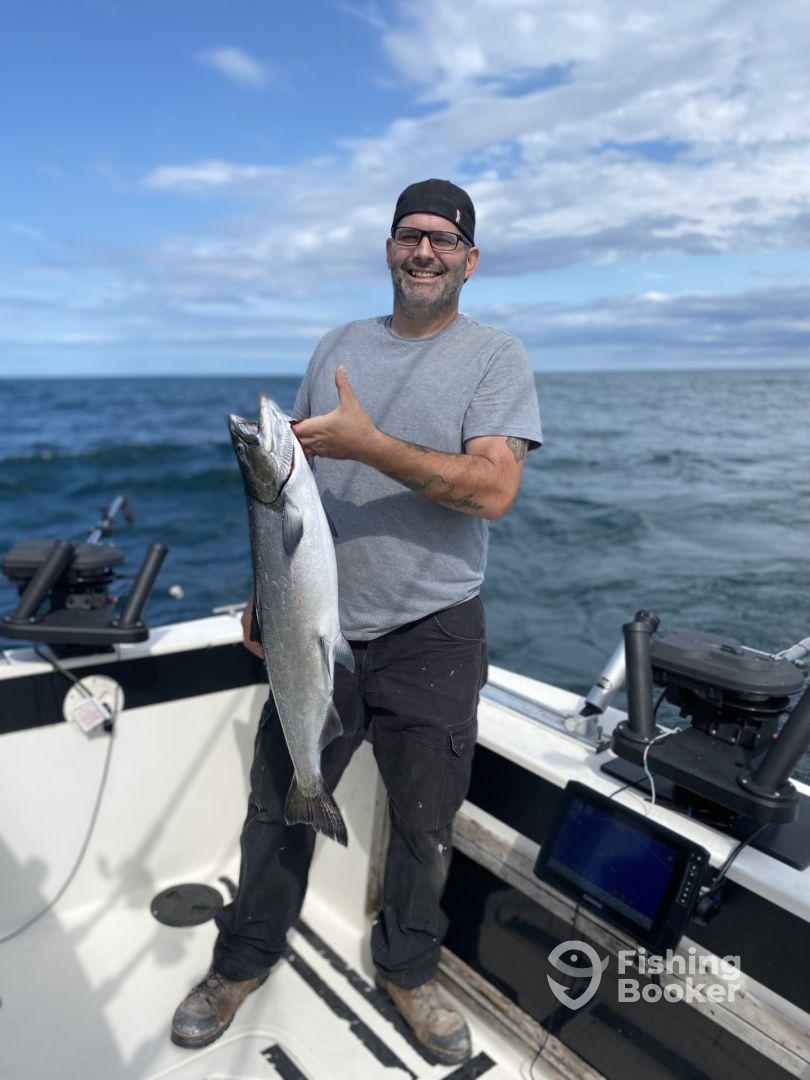 An angler proudly displaying a large Salmon while fishing on a boat in open waters.