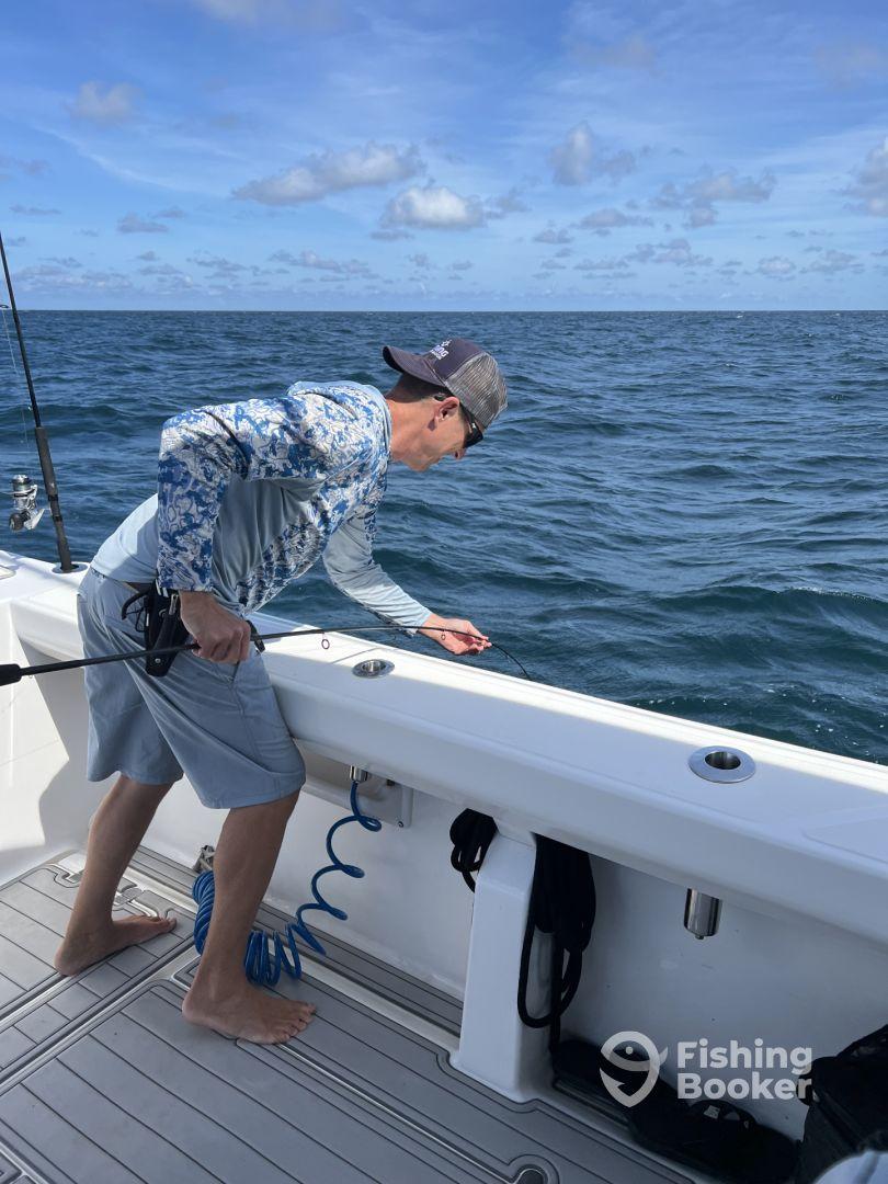 An angler casting a line off the side of a sport fishing boat in open waters, showcasing the excitement of deep-sea fishing.