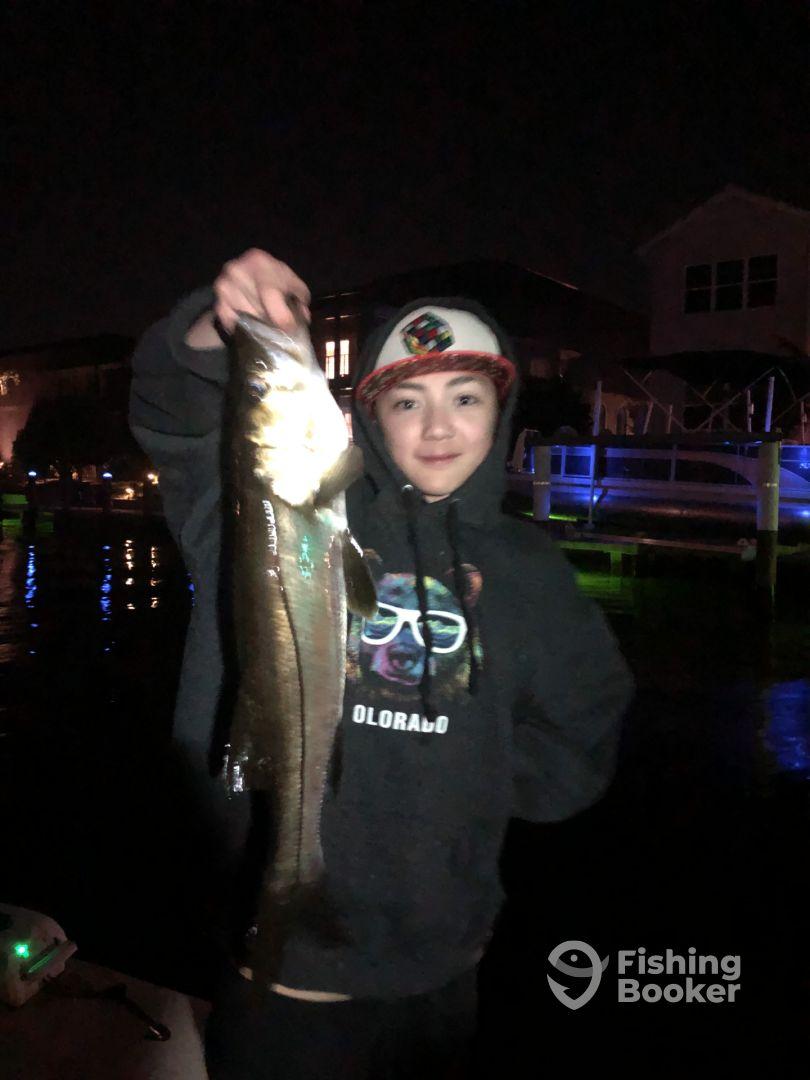 A young angler proudly displaying a caught fish at night, showcasing a successful fishing experience on the water.