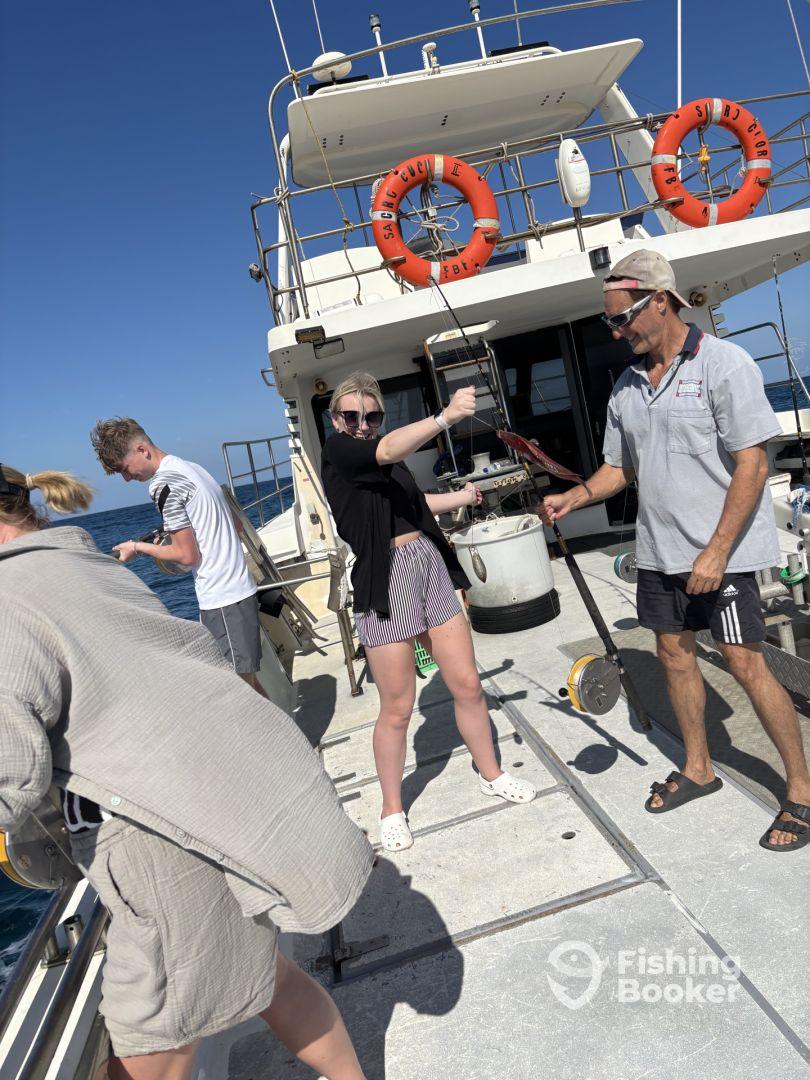 A group of anglers actively fishing on a charter boat, with one young woman reeling in a catch while others assist, showcasing a vibrant day on the water.