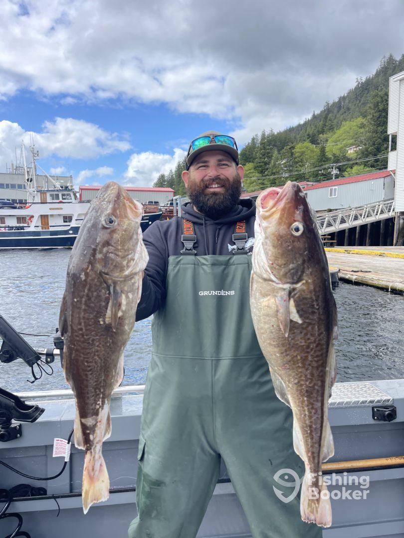Angler proudly displaying two large Cod caught during a fishing trip in a scenic coastal environment.