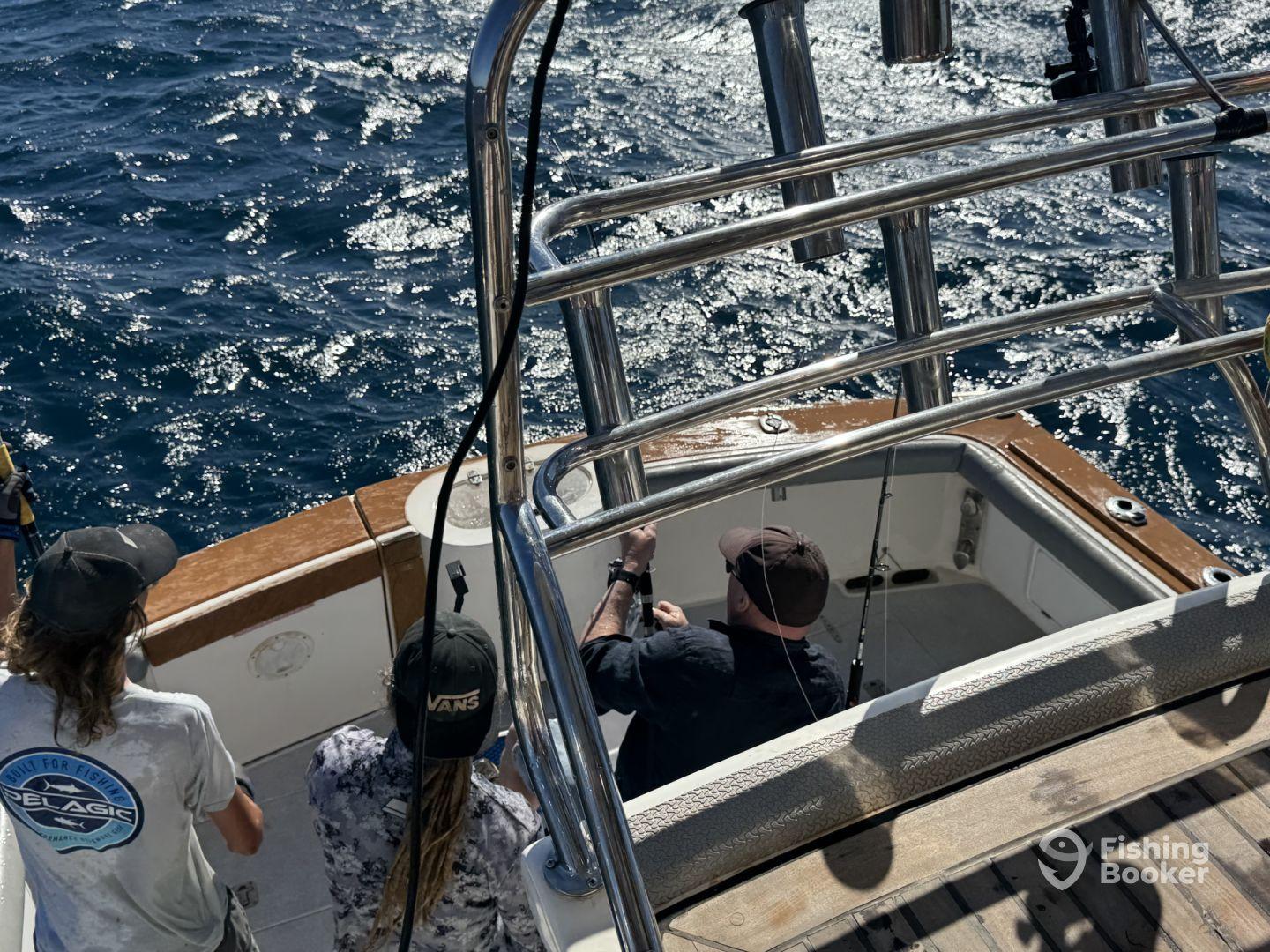 Three anglers aboard a fishing boat, actively engaged in reeling in a catch while enjoying a sunny day on the open water.