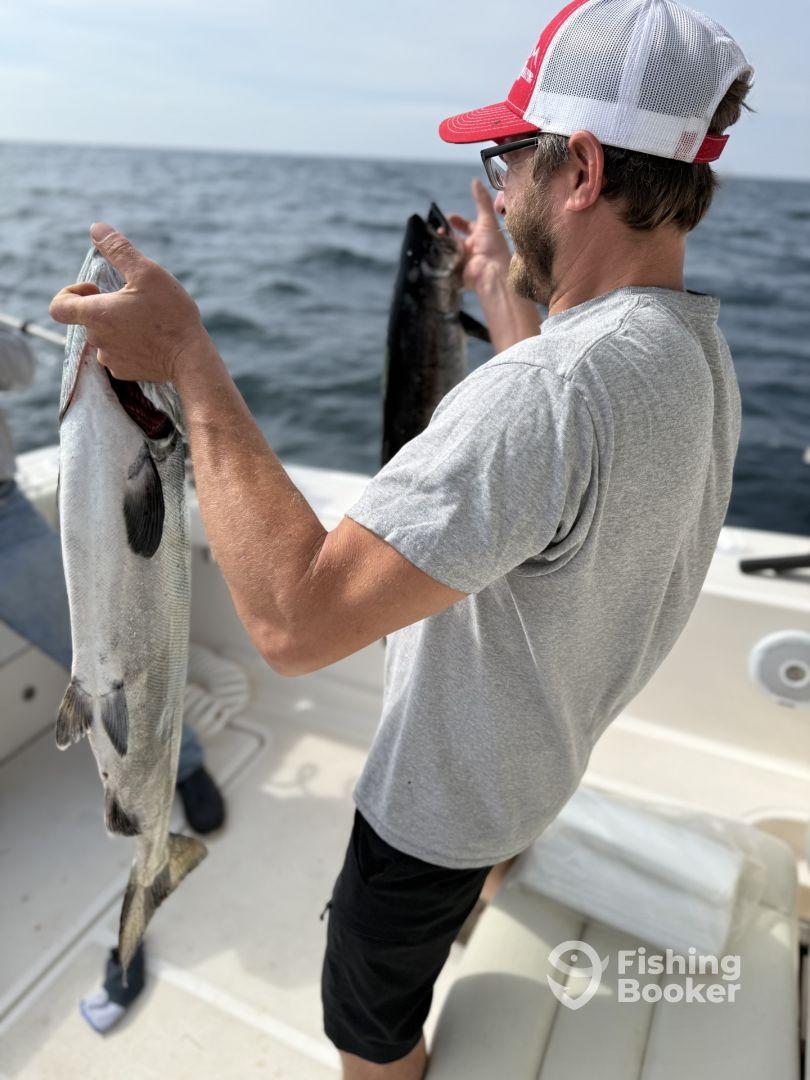 An angler proudly displaying two fish, including a large salmon, while fishing on a boat in open water.