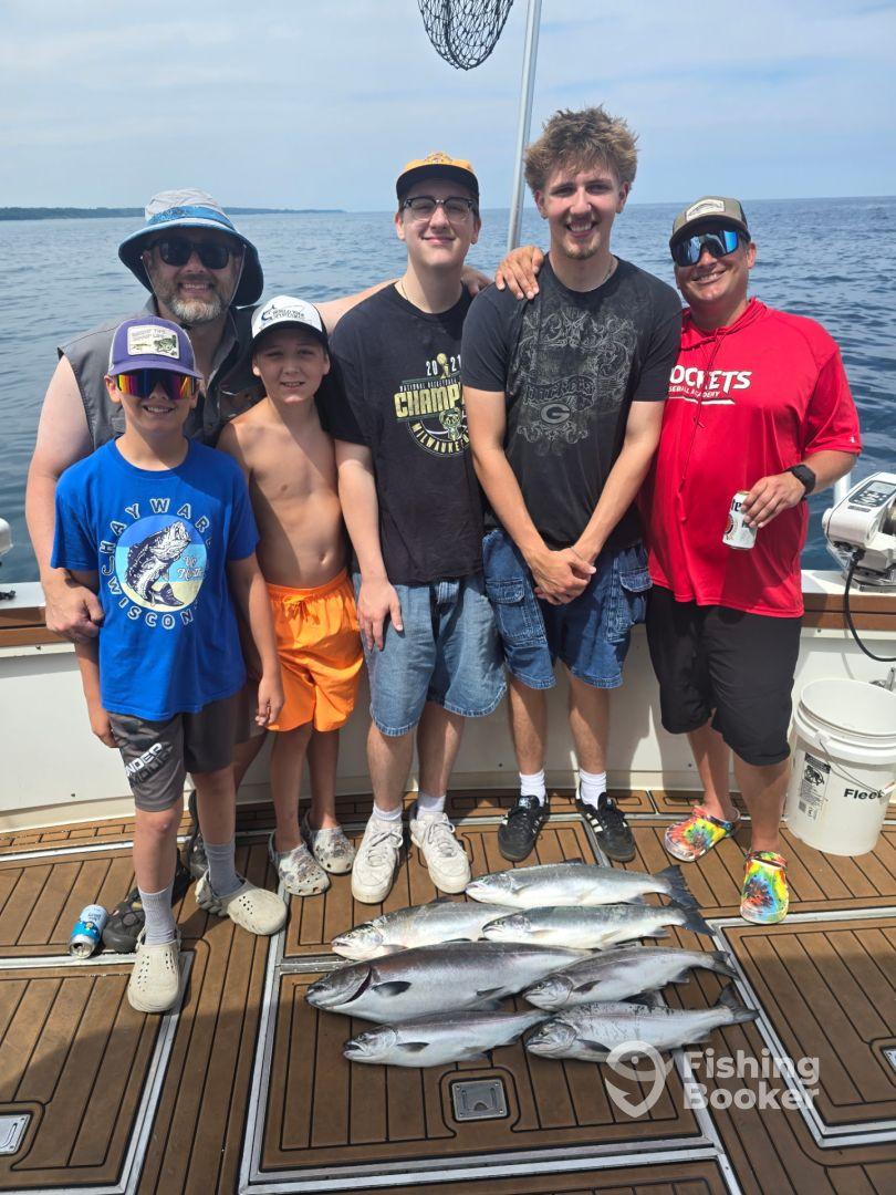 A family group proudly displaying their catch of multiple fish on the deck of a fishing boat, enjoying a day out on the water.