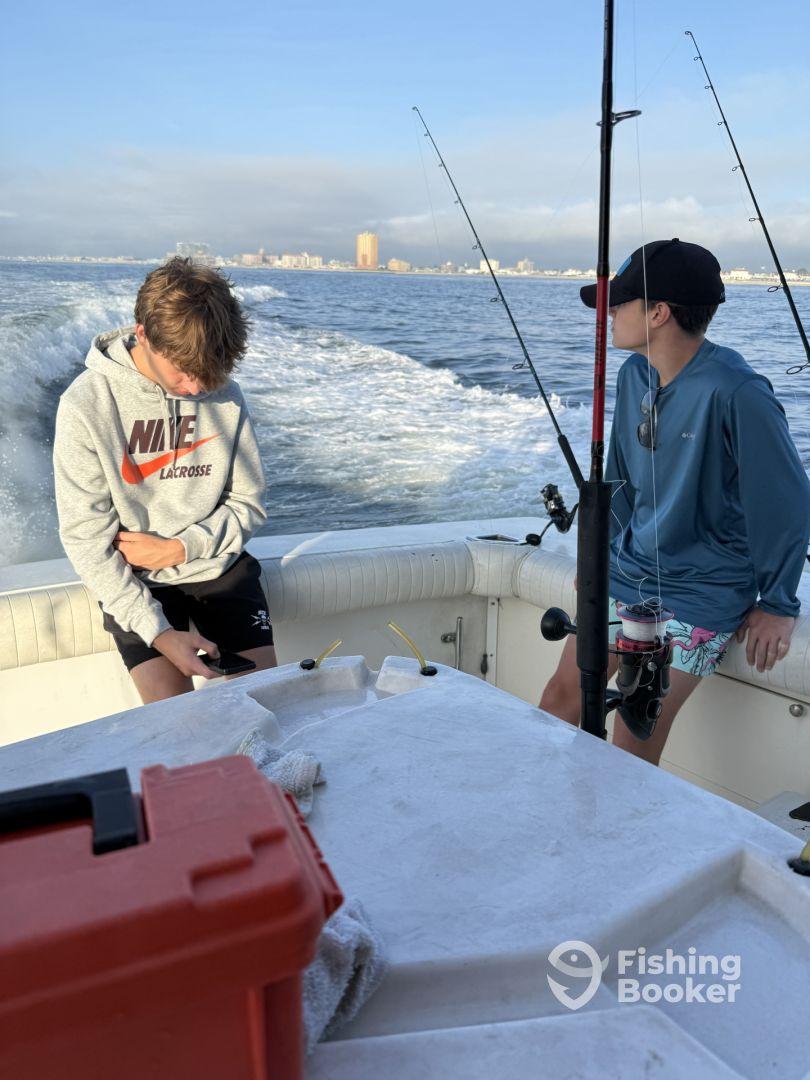 Two young anglers seated inside a boat, preparing for a fishing trip with city skyline in the background.
