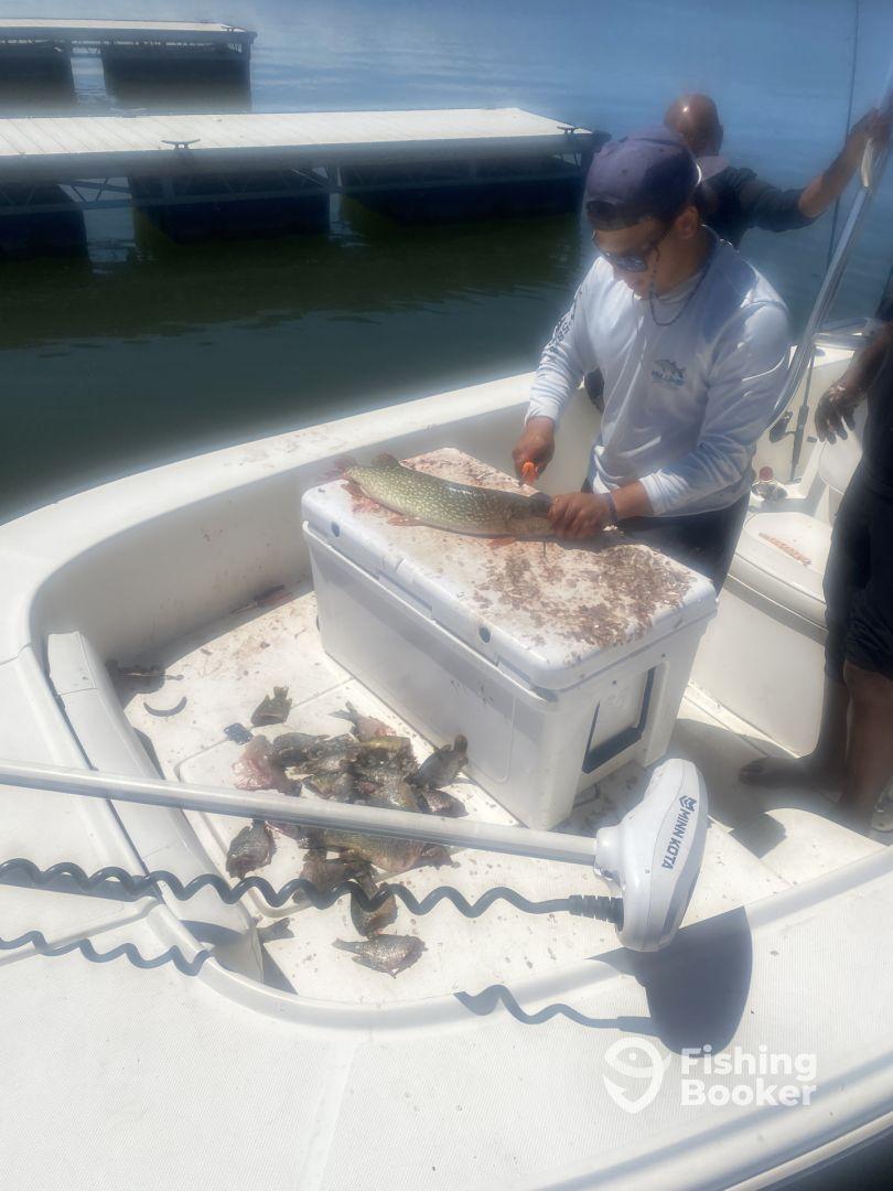 A fisherman filleting a large fish on a boat, surrounded by smaller fish on the deck, showcasing a productive day on the water.