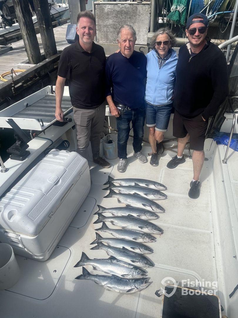 A group of four anglers proudly displaying their catch of salmon on the deck of a fishing boat, showcasing a successful day on the water.