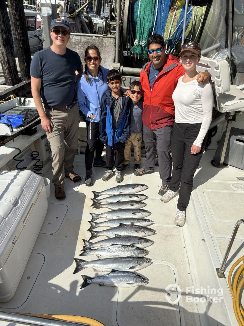 A family group proudly displaying their catch of salmon on the deck of a fishing boat, showcasing a successful day on the water.