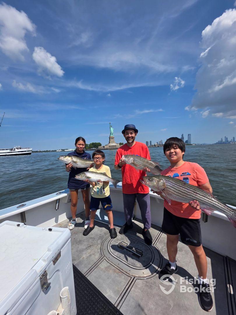 A family proudly displaying their catch of striped bass while enjoying a fishing trip near the Statue of Liberty.
