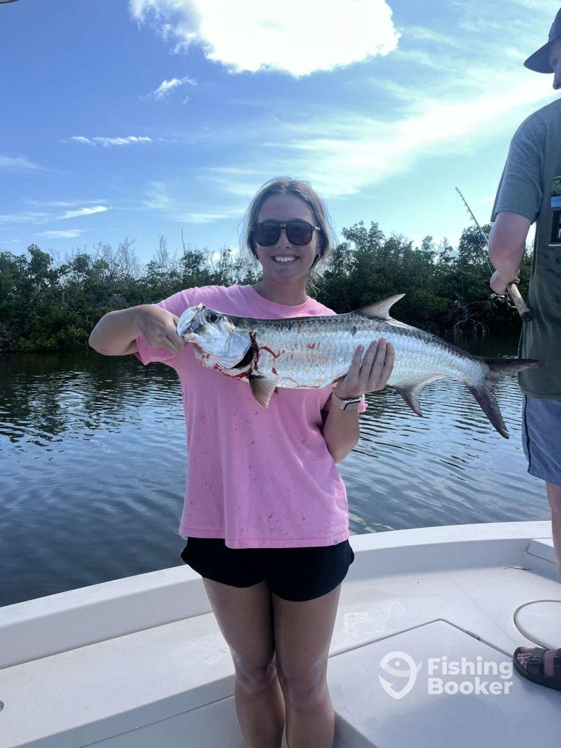 A proud angler displaying a large Tarpon while fishing on a boat in a scenic coastal environment.