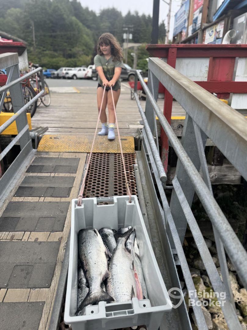 A young girl pulling a cooler filled with freshly caught salmon at a fishing dock, showcasing the excitement of a successful fishing trip.