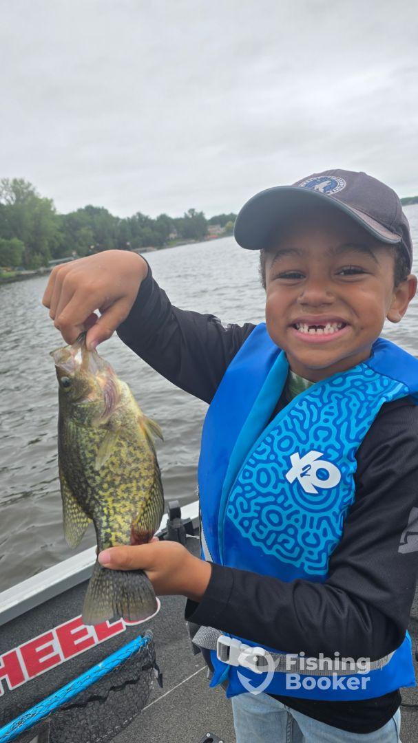 A young angler proudly displaying a Crappie while fishing on a lake, showcasing a fun day on the water.