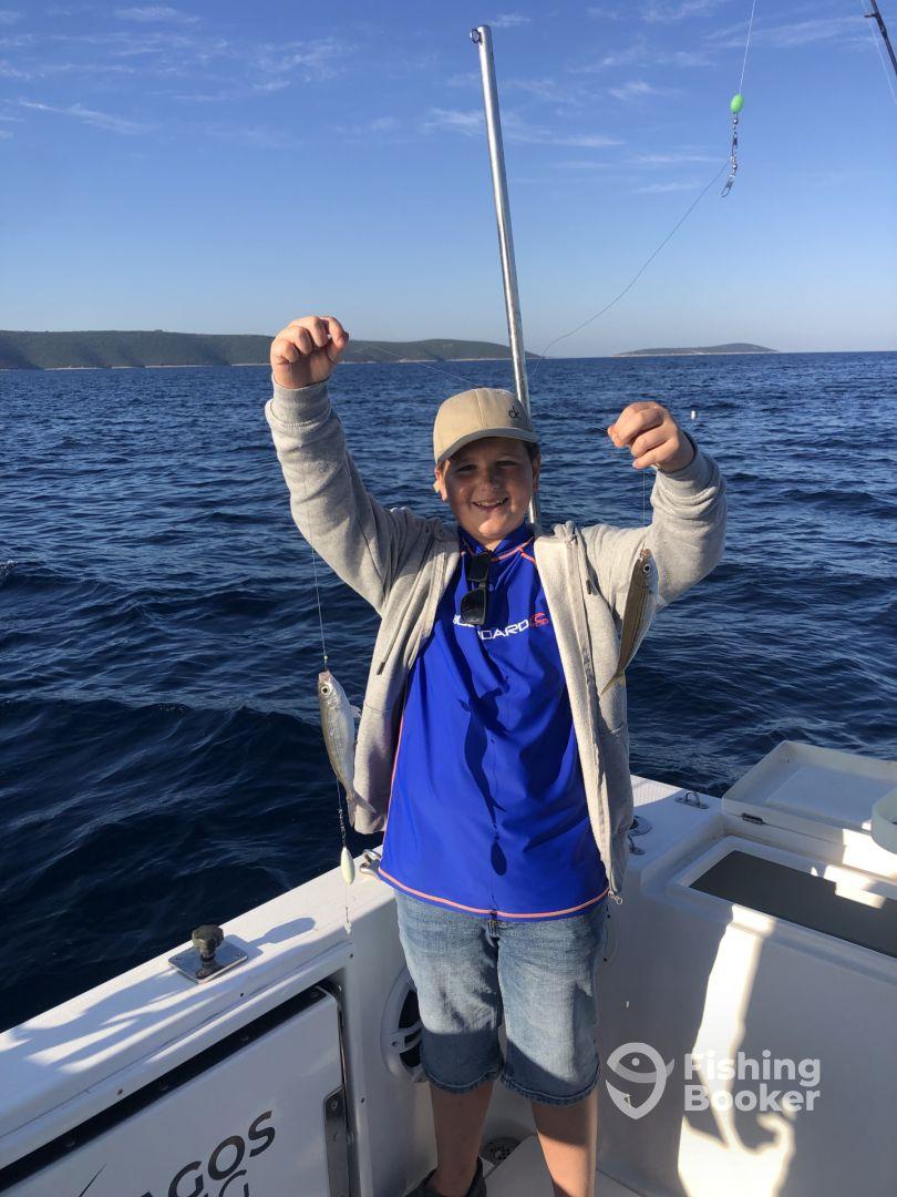 A young angler proudly displaying his catch while fishing on a boat in clear blue waters.