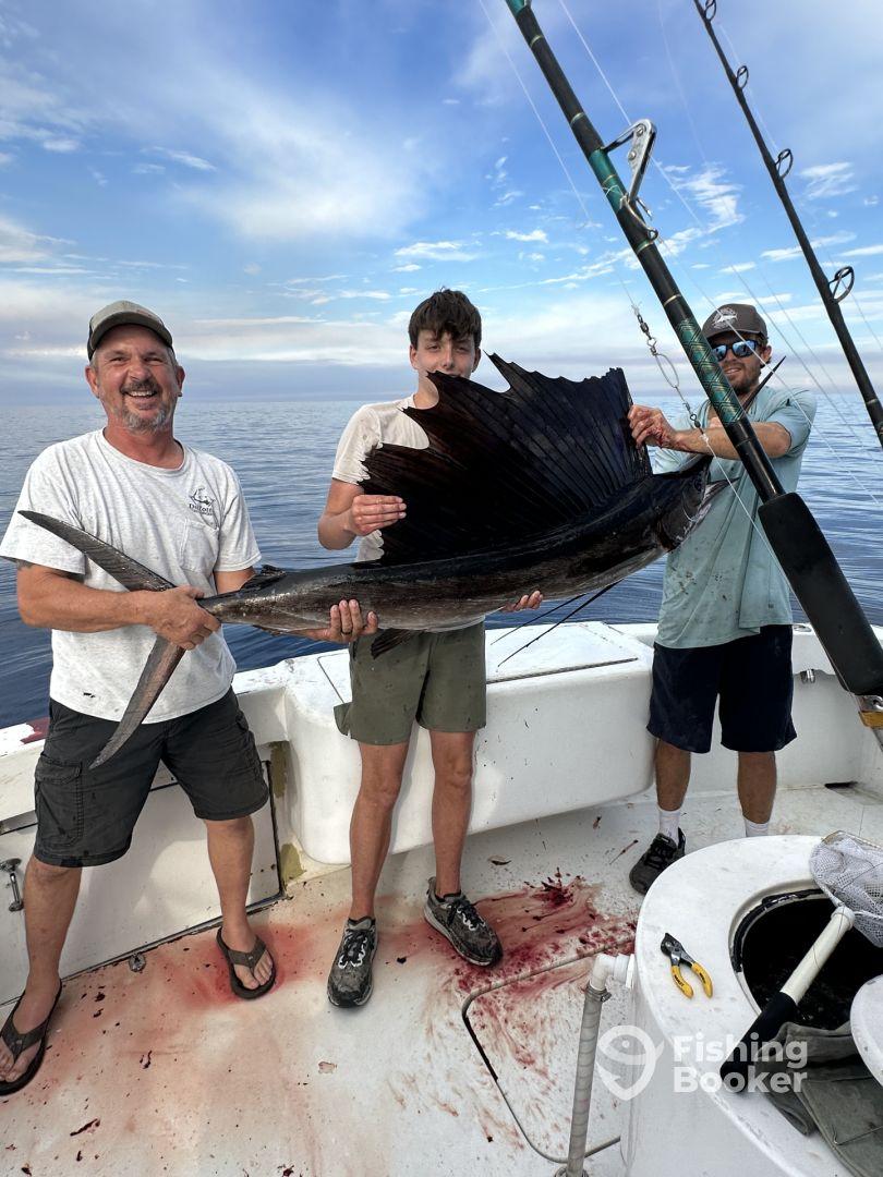 A group of anglers proudly displaying a large Sailfish aboard a fishing charter in calm waters, showcasing a successful day on the ocean.