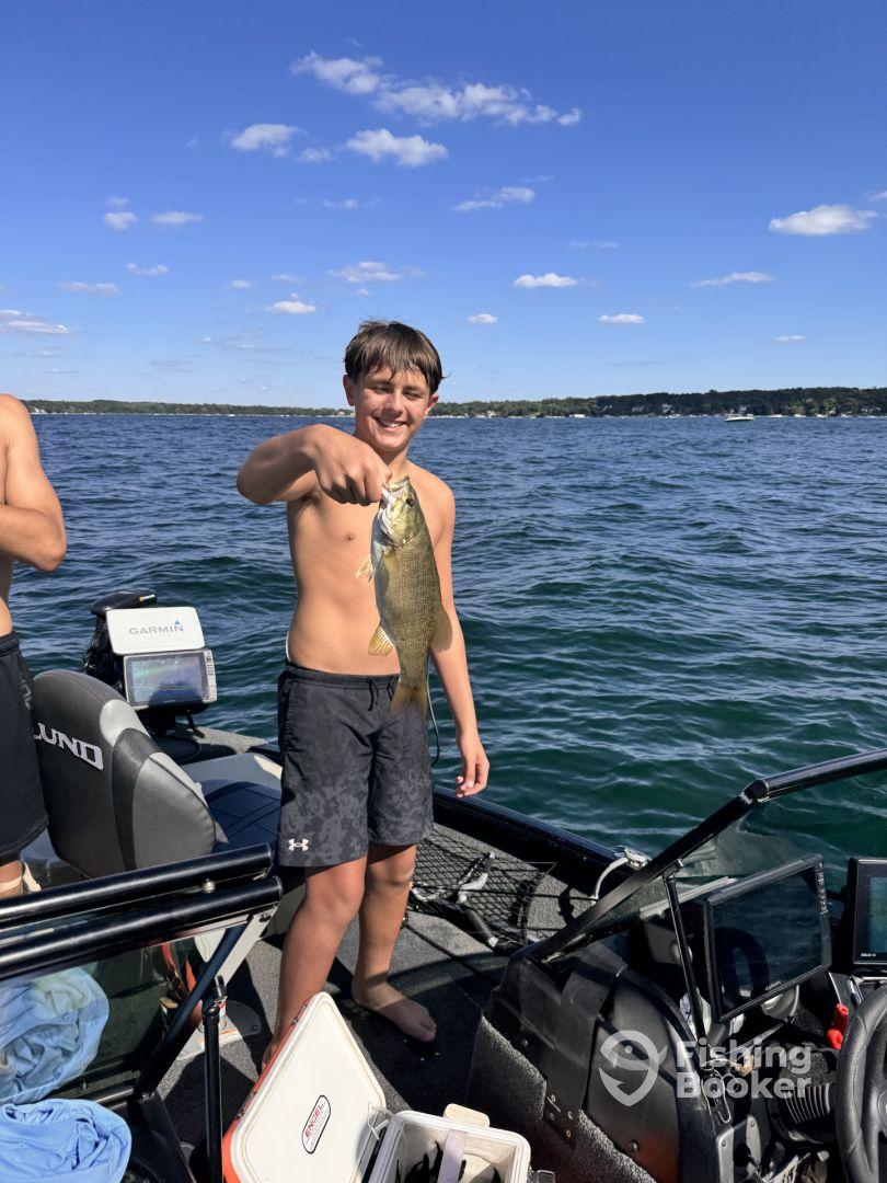 A young angler proudly displaying a caught fish while fishing on a boat, enjoying a sunny day on the water.