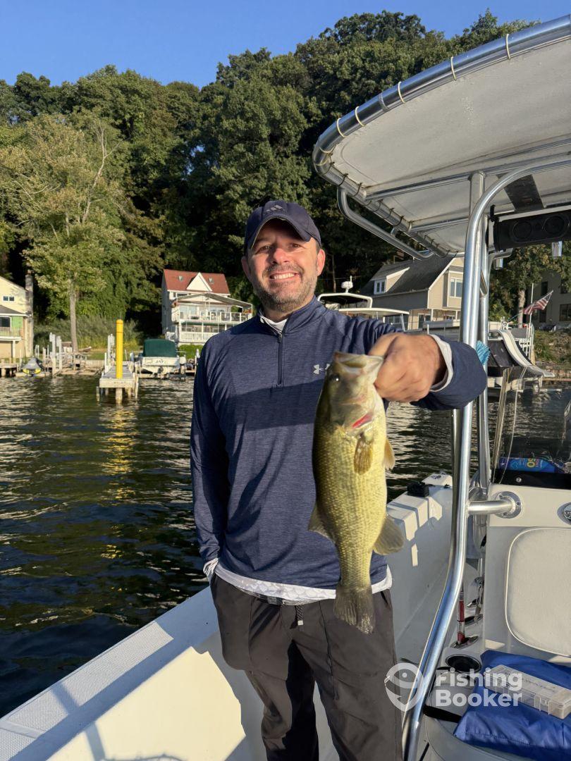 An angler proudly displaying a large Largemouth Bass while on a boat, with a scenic lakeside background.