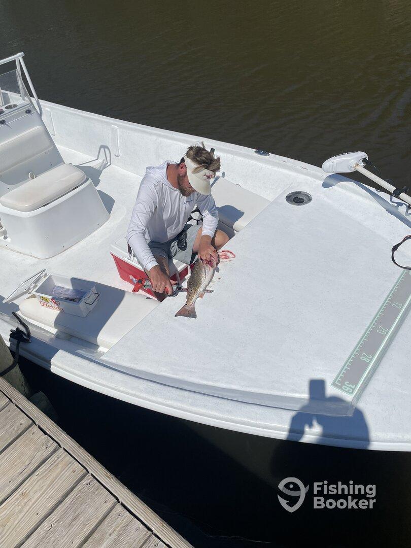 Angler preparing a freshly caught fish on the deck of a boat, showcasing a typical day of fishing in a calm water environment.