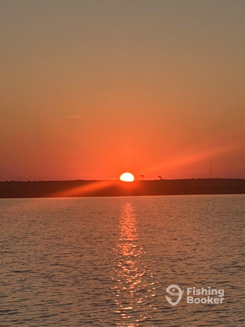 A stunning sunset over the water, casting a warm glow and reflections on the surface, creating a serene fishing environment.