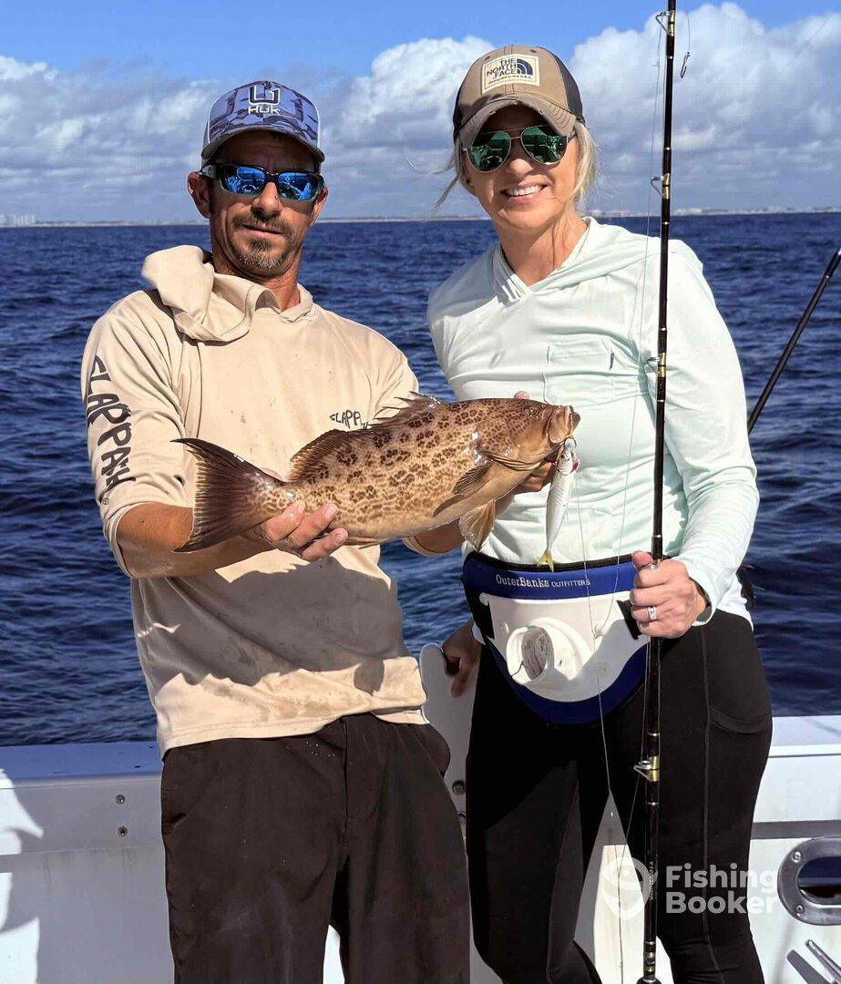 Two anglers proudly displaying a large Grouper while fishing on a charter boat in clear blue waters.