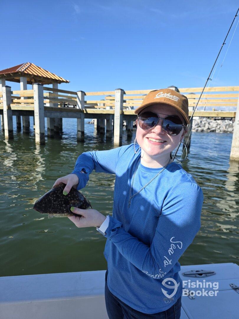 A young angler proudly displaying a flounder while fishing near a dock on a sunny day.
