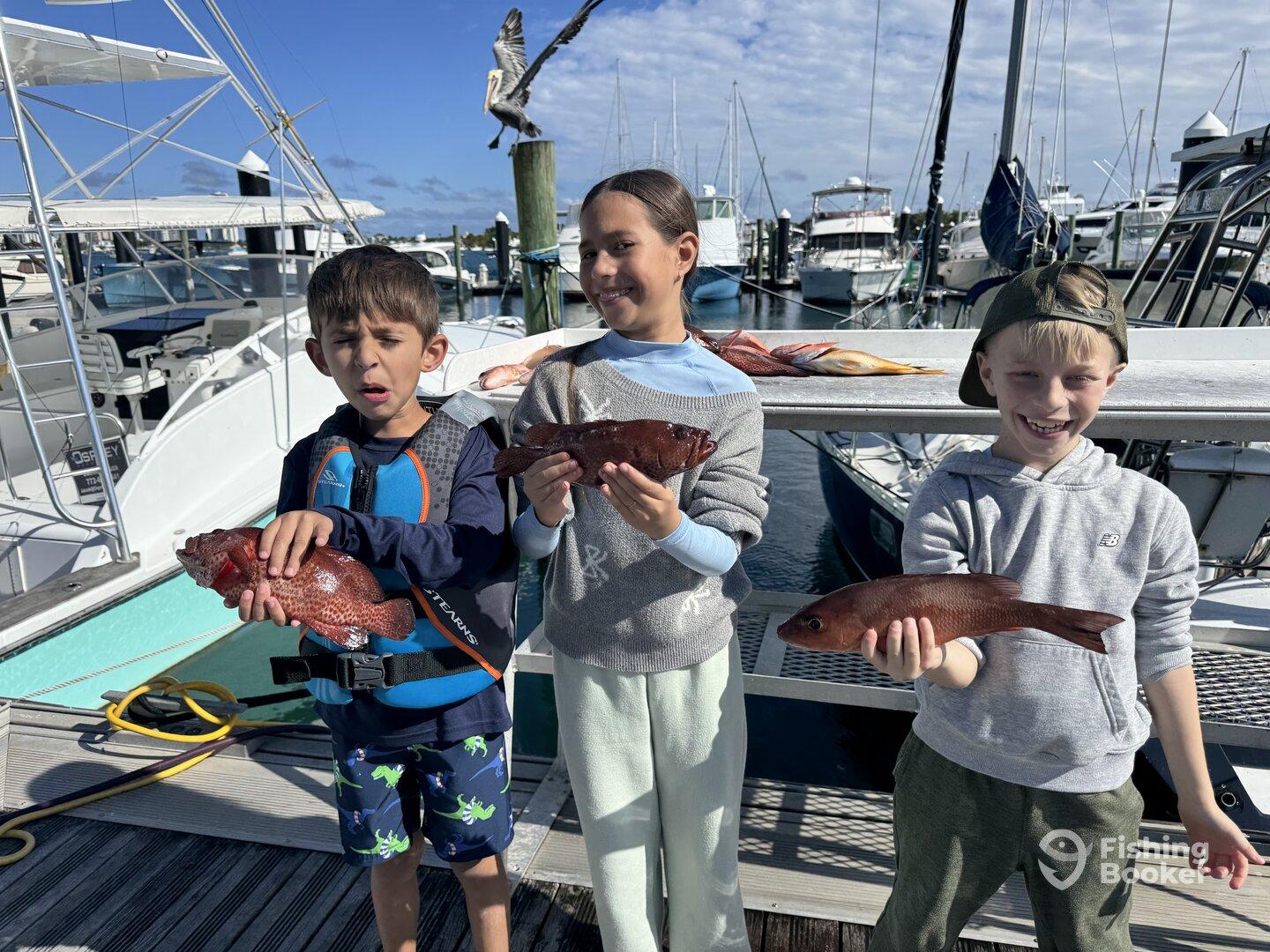 Three young anglers proudly displaying their catches of colorful snapper at the marina after a fun-filled fishing trip.
