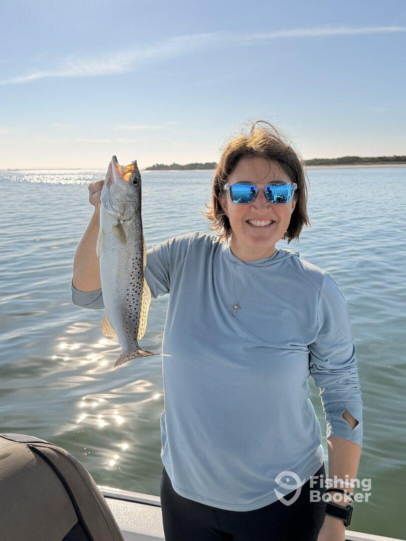 A proud angler holding a Speckled Trout while enjoying a sunny day on the water.