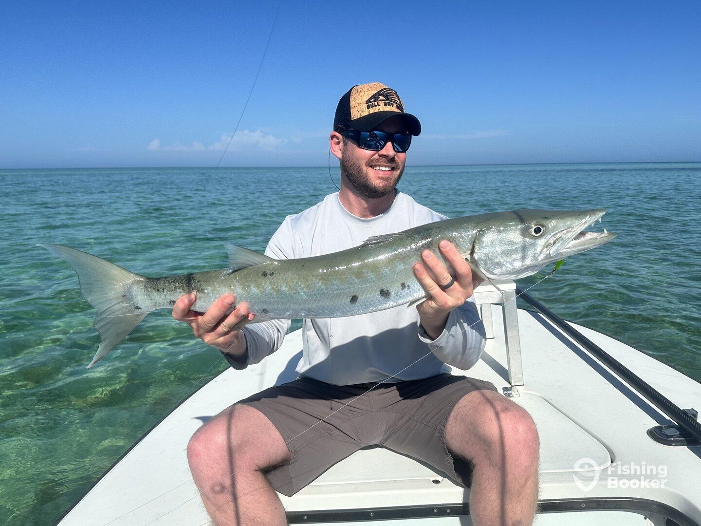 Angler proudly displaying a large Barracuda while fishing in clear waters, showcasing a successful day on the boat.