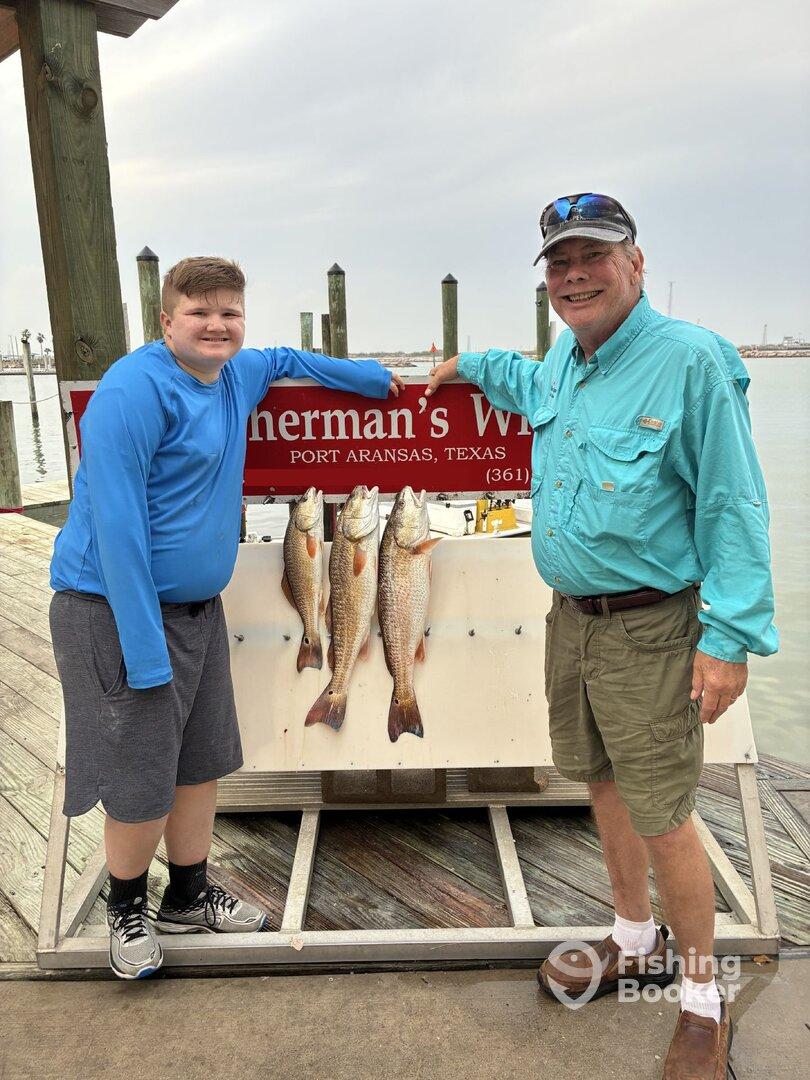 A young angler and an adult proudly display their catch of Redfish at the dock in Port Aransas, Texas.