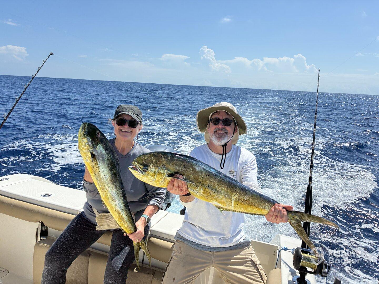 Two anglers proudly displaying their Mahi Mahi catch while enjoying a sunny day on the open ocean.