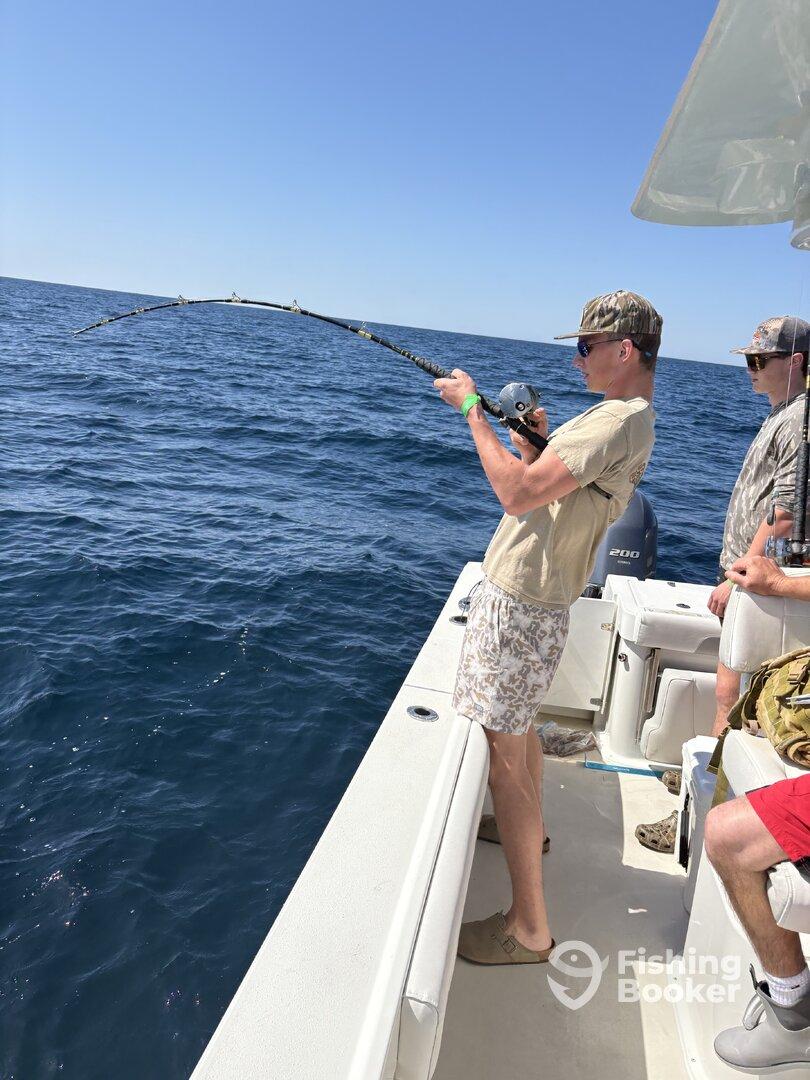 A young angler is reeling in a fish while fishing on a boat in open waters, showcasing the excitement of deep-sea fishing.