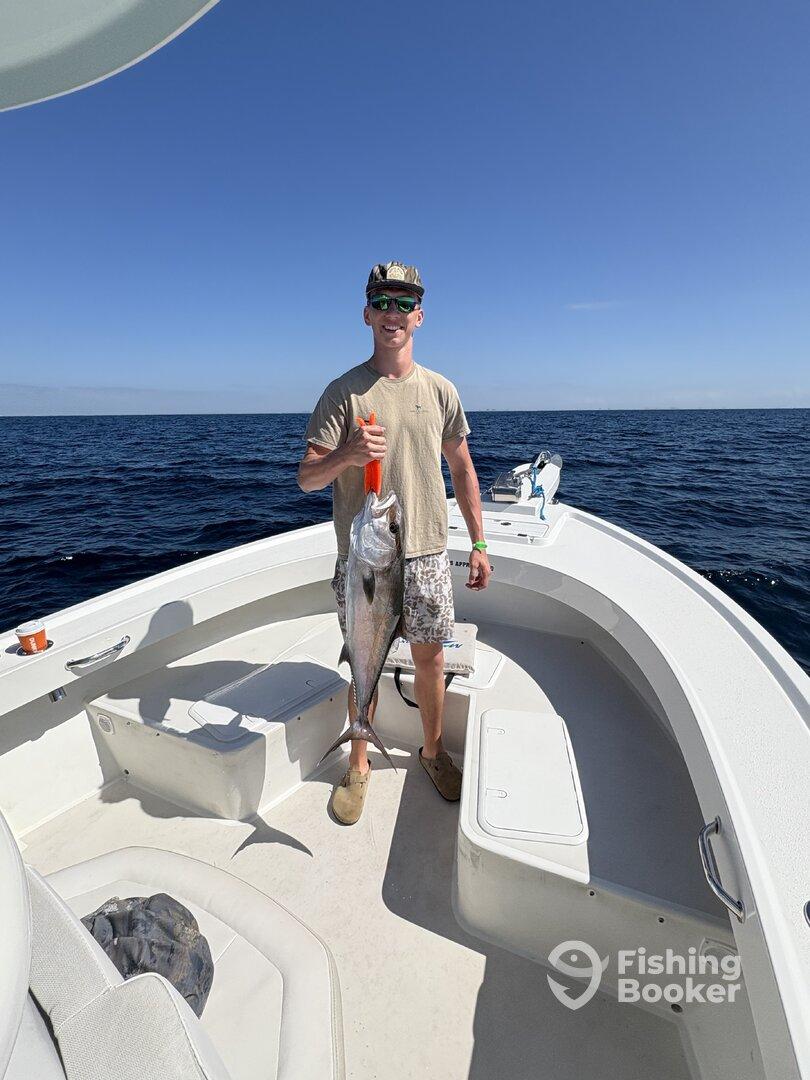 Angler proudly displaying a large fish on a boat during a deep-sea fishing trip.