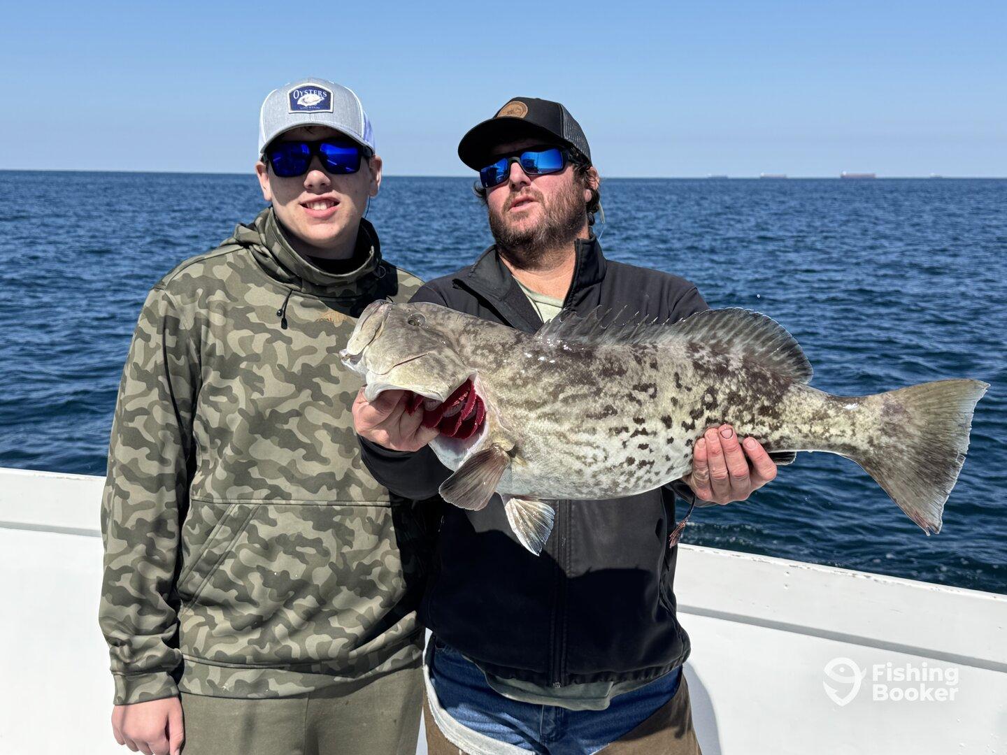 Two anglers proudly displaying a large Grouper while fishing offshore, showcasing a successful day on the water.