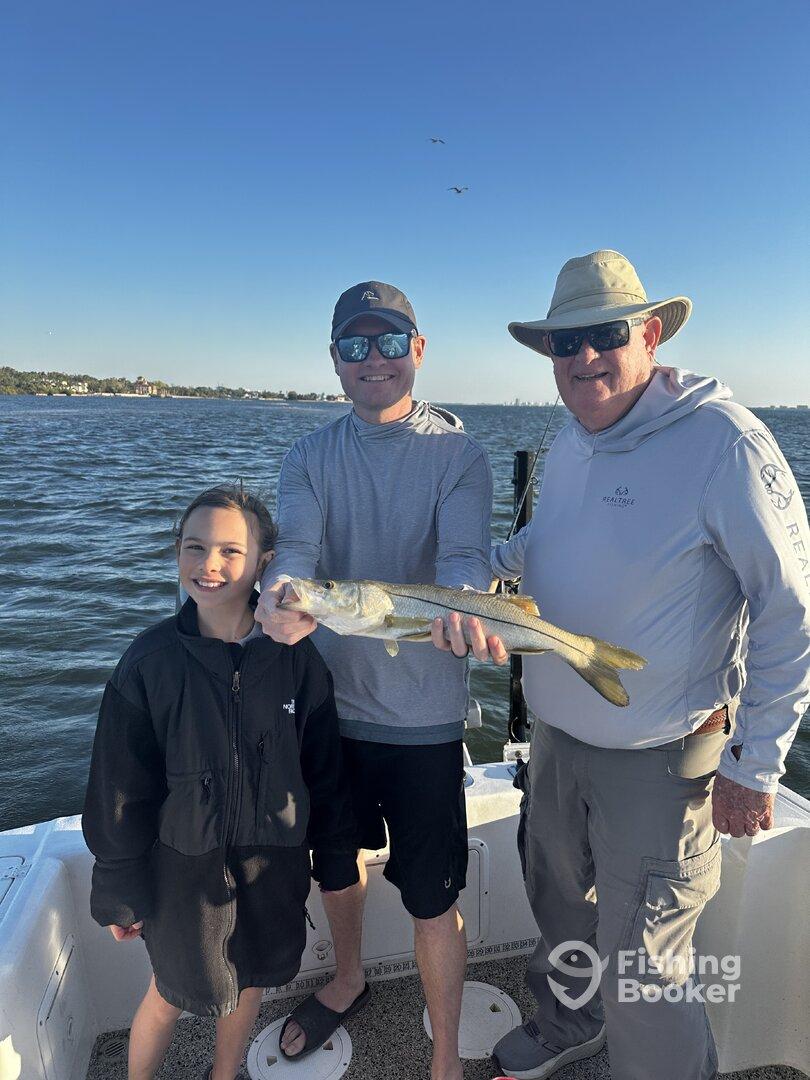 A family proudly displays a caught Snook while fishing on a boat, enjoying a sunny day on the water.